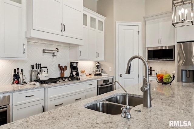 kitchen featuring stainless steel appliances, premium range hood, a sink, white cabinets, and decorative backsplash