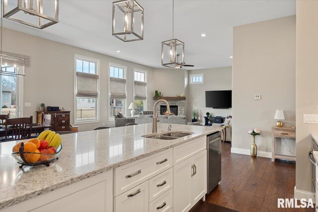 kitchen with a stone fireplace, dark wood-style flooring, a sink, hanging light fixtures, and dishwasher