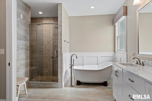 bathroom featuring a wainscoted wall, a decorative wall, a stall shower, vanity, and a freestanding tub