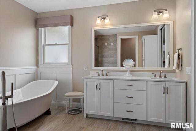 full bathroom featuring double vanity, a freestanding tub, a sink, and wood finished floors