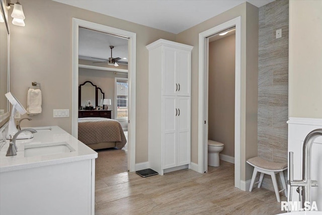 bathroom with ensuite bathroom, toilet, wood finished floors, a sink, and a ceiling fan