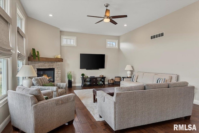 living room with a stone fireplace, recessed lighting, dark wood-style flooring, visible vents, and baseboards