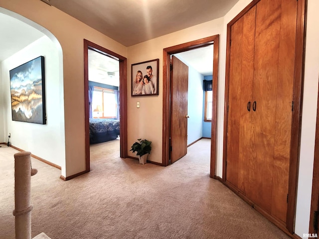 hall featuring arched walkways, light colored carpet, and baseboards