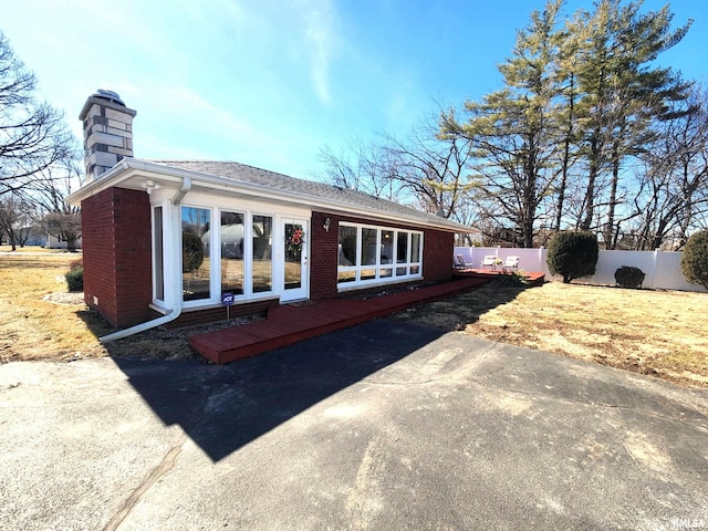 exterior space featuring a wooden deck, a chimney, fence, and brick siding