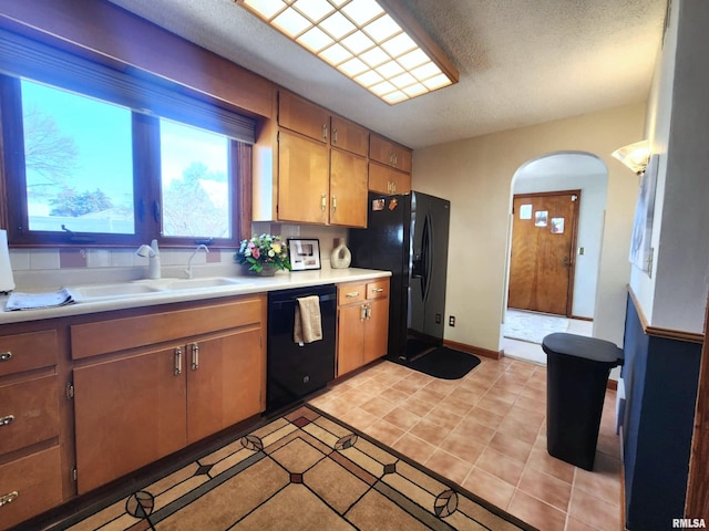 kitchen featuring arched walkways, light tile patterned flooring, a sink, light countertops, and black appliances