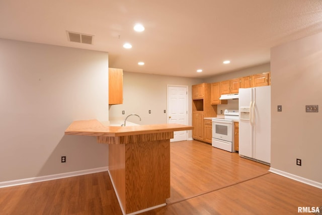 kitchen featuring a breakfast bar area, light wood-style flooring, a peninsula, white appliances, and visible vents