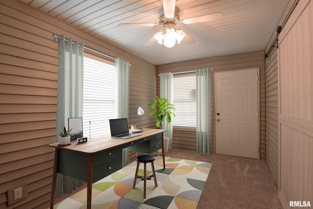 carpeted office space featuring a barn door, wood walls, and a ceiling fan