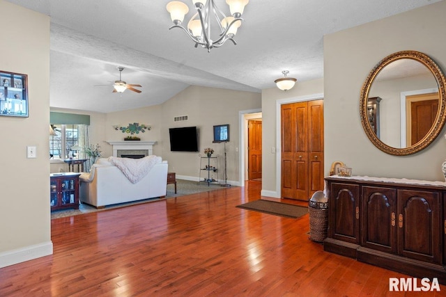 living area with a fireplace, vaulted ceiling, wood finished floors, and ceiling fan with notable chandelier