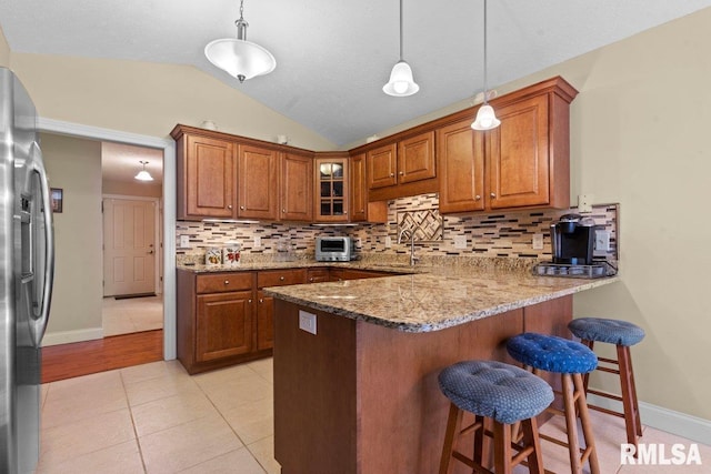 kitchen featuring brown cabinetry, light stone counters, stainless steel refrigerator with ice dispenser, and a peninsula