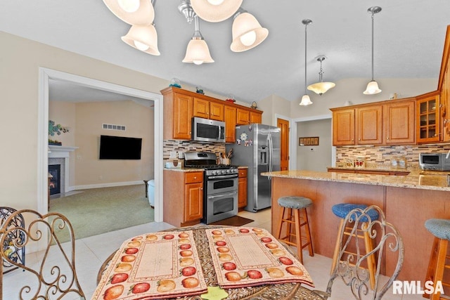 kitchen featuring stainless steel appliances, lofted ceiling, a kitchen breakfast bar, and light stone countertops