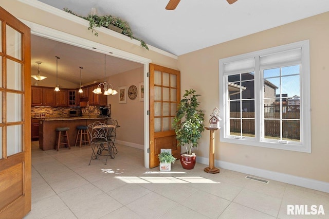 unfurnished dining area featuring lofted ceiling, light tile patterned floors, ceiling fan with notable chandelier, visible vents, and baseboards