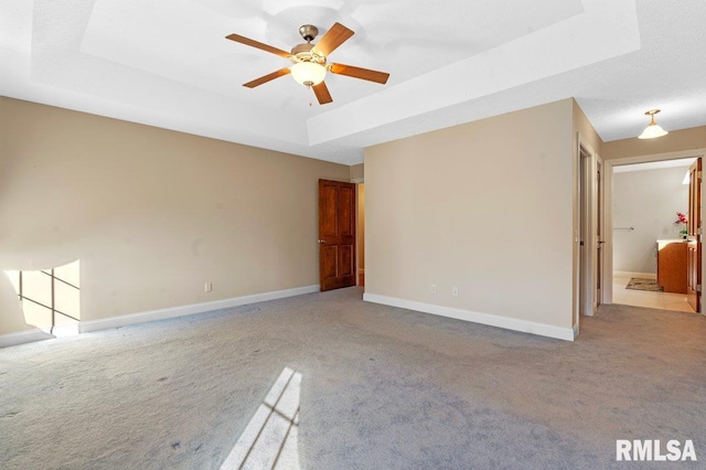 carpeted empty room with a ceiling fan, a raised ceiling, and baseboards