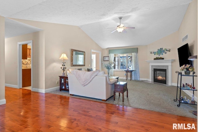 living area with visible vents, a ceiling fan, a fireplace with flush hearth, vaulted ceiling, and wood finished floors