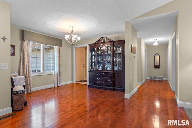 unfurnished dining area with visible vents, a textured ceiling, hardwood / wood-style floors, and an inviting chandelier