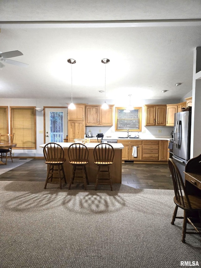 kitchen featuring a kitchen breakfast bar, hanging light fixtures, light countertops, stainless steel refrigerator with ice dispenser, and a sink