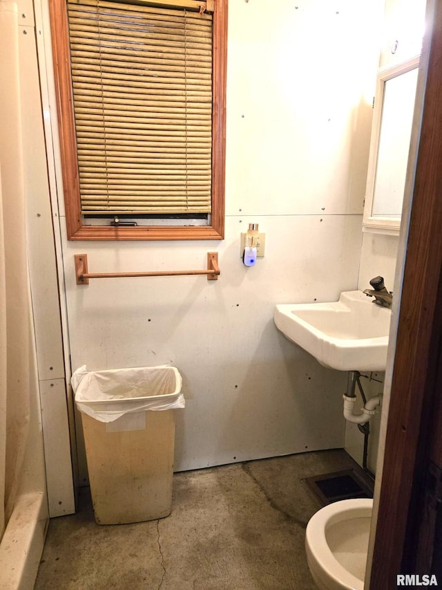 bathroom with unfinished concrete flooring, a sink, and toilet