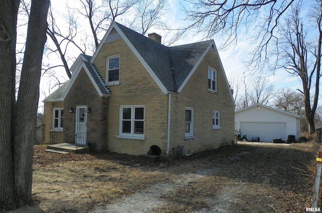 view of front of house featuring brick siding, a shingled roof, an outdoor structure, a detached garage, and a chimney