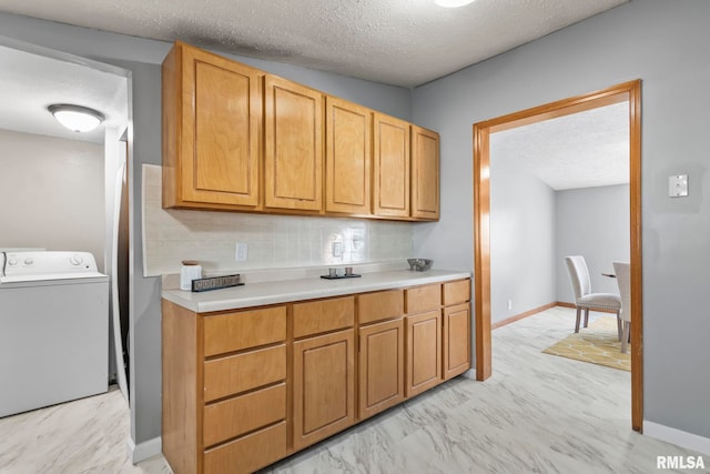 kitchen with washer / dryer, baseboards, marble finish floor, light countertops, and a textured ceiling
