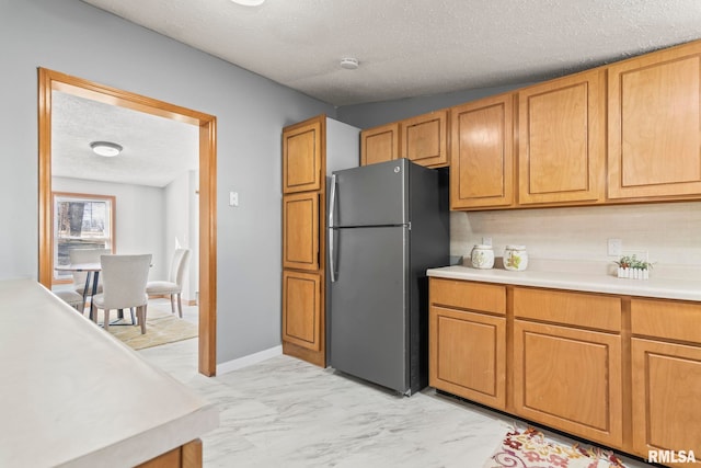 kitchen with marble finish floor, light countertops, brown cabinetry, freestanding refrigerator, and a textured ceiling