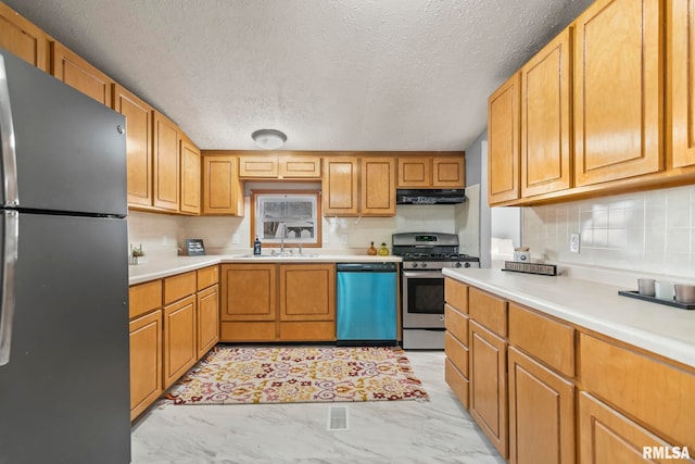 kitchen featuring appliances with stainless steel finishes, marble finish floor, light countertops, under cabinet range hood, and a sink