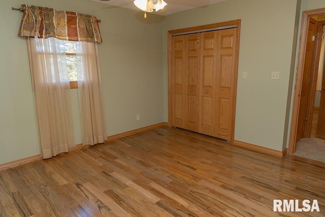 unfurnished bedroom featuring a ceiling fan, a closet, light wood-style flooring, and baseboards