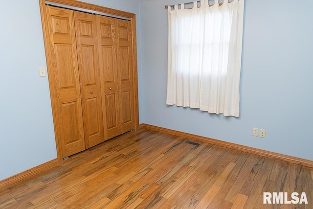 unfurnished bedroom with a closet, wood finished floors, visible vents, and baseboards