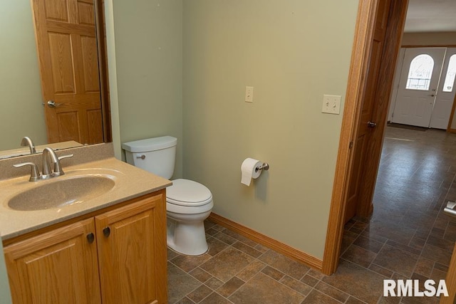 bathroom featuring stone finish flooring, baseboards, vanity, and toilet