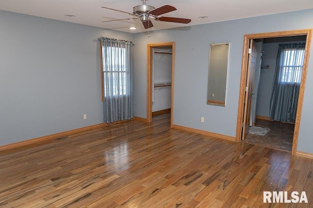 unfurnished bedroom with multiple windows, a spacious closet, baseboards, and wood finished floors