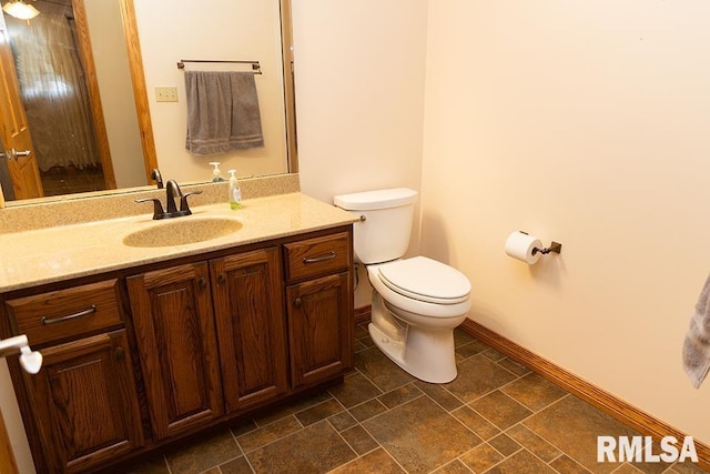 bathroom featuring stone finish flooring, baseboards, vanity, and toilet