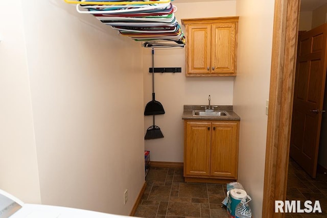 laundry room with indoor wet bar, cabinet space, stone finish flooring, a sink, and baseboards