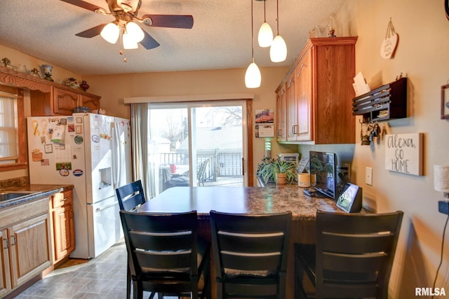 kitchen with a textured ceiling, white fridge with ice dispenser, a peninsula, and brown cabinets