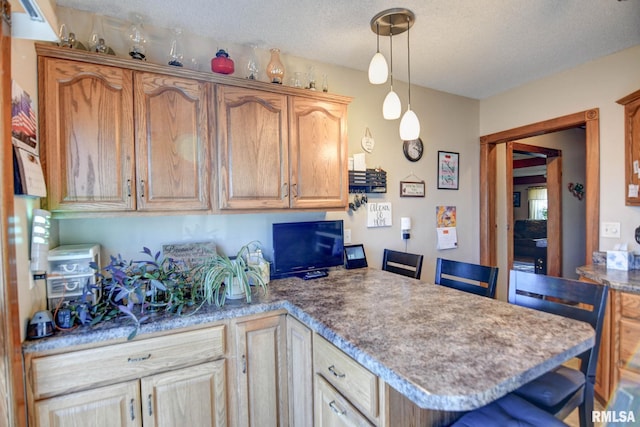 kitchen featuring a peninsula, a breakfast bar area, a textured ceiling, and decorative light fixtures