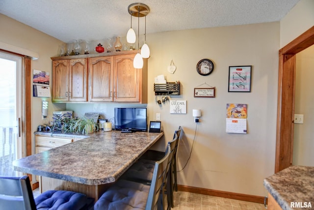 kitchen featuring baseboards, a breakfast bar, decorative light fixtures, a peninsula, and a textured ceiling