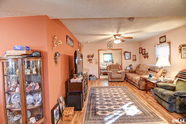 living room with ceiling fan, light wood-style flooring, and a textured ceiling