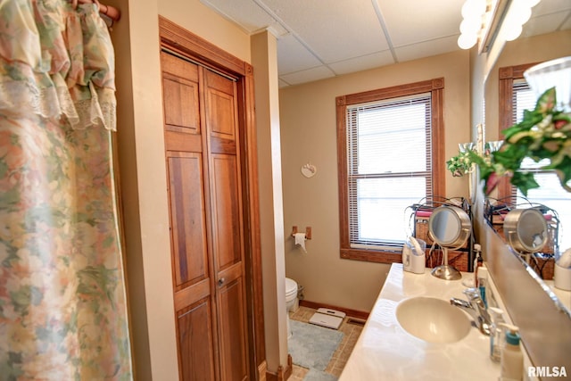 bathroom with baseboards, toilet, vanity, a paneled ceiling, and a closet