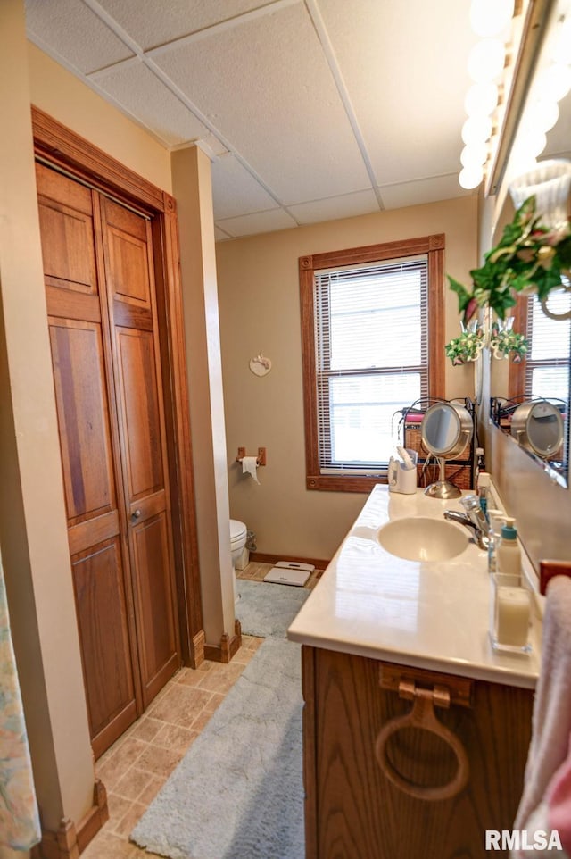 bathroom with a paneled ceiling, baseboards, toilet, and vanity