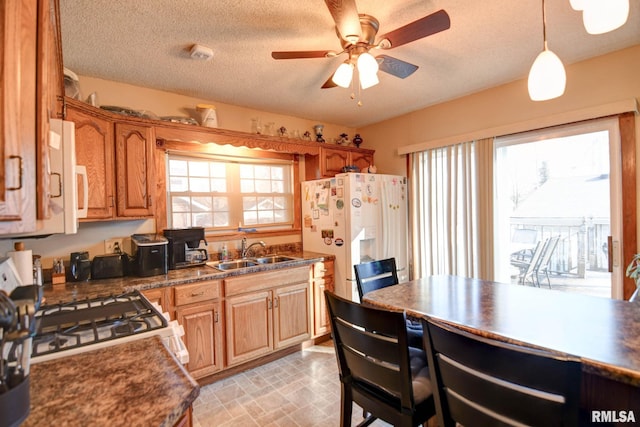 kitchen featuring a ceiling fan, dark countertops, white refrigerator with ice dispenser, and a sink