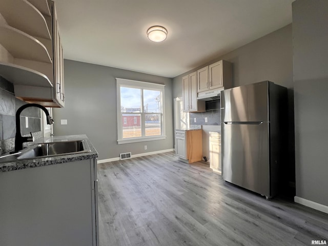 kitchen featuring tasteful backsplash, freestanding refrigerator, a sink, light wood-type flooring, and baseboards