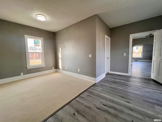 spare room featuring plenty of natural light, visible vents, baseboards, and wood finished floors