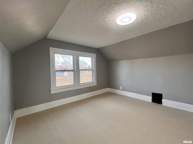 additional living space with baseboards, vaulted ceiling, a textured ceiling, and carpet flooring