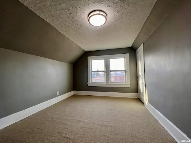 additional living space with carpet floors, baseboards, vaulted ceiling, and a textured ceiling