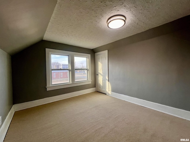 additional living space with a textured ceiling, light carpet, lofted ceiling, and baseboards