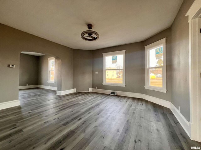 spare room with arched walkways, dark wood-style floors, visible vents, and baseboards