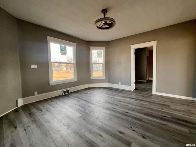 empty room featuring visible vents, dark wood finished floors, and baseboards