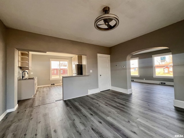 unfurnished living room featuring arched walkways, a healthy amount of sunlight, visible vents, and dark wood finished floors