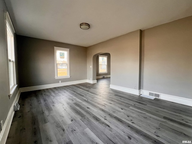 unfurnished room featuring baseboards, arched walkways, and wood finished floors