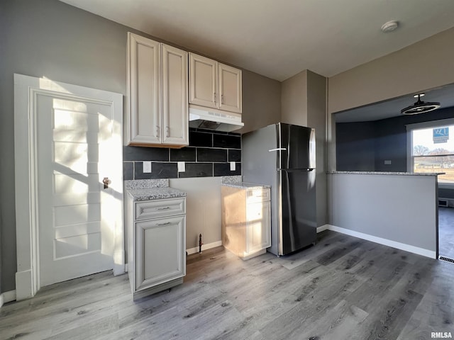 kitchen with tasteful backsplash, baseboards, light wood-style flooring, freestanding refrigerator, and under cabinet range hood