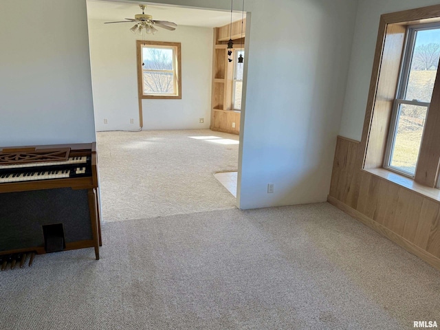 carpeted spare room featuring wainscoting, ceiling fan, and wooden walls