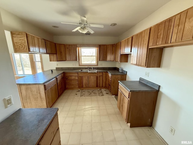 kitchen featuring a ceiling fan, dark countertops, brown cabinets, a peninsula, and a sink