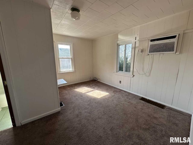 unfurnished room with carpet floors, a wall unit AC, visible vents, and baseboards